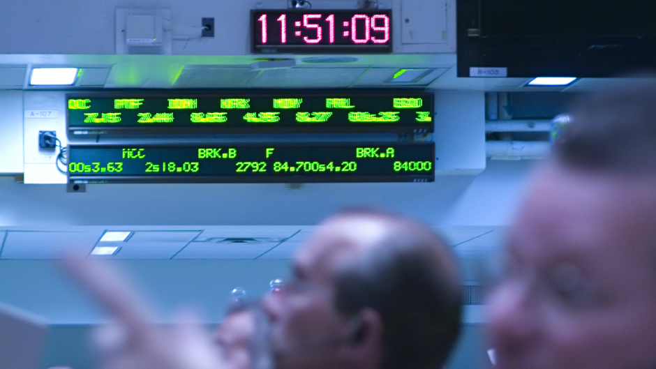 Analistas do mercado financeiro na mesa de operação, observando painel de bolsas