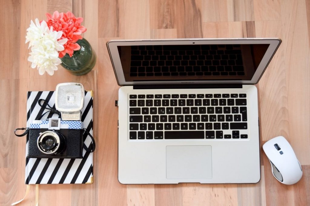 objetos vistos de cima: notebook, mouse, câmera e vaso de flores